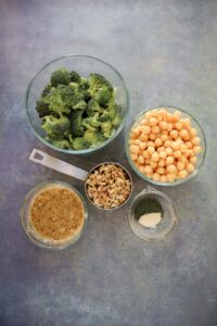 top down pic of bowls of broccoli, chickpeas, walnuts, maple mustard dressing and spices
