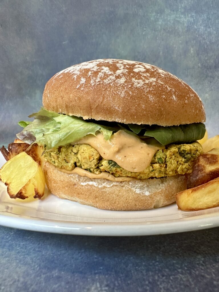 Chickpea basil burger on a bun with roasted potatoes on a white plate