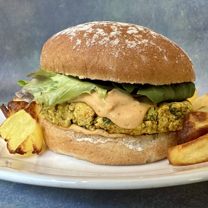 Chickpea basil burger on a bun with roasted potatoes on a white plate