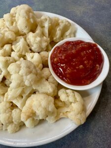 Boiled Cauliflower on a white plate with a side of ketchup based cocktail sauce