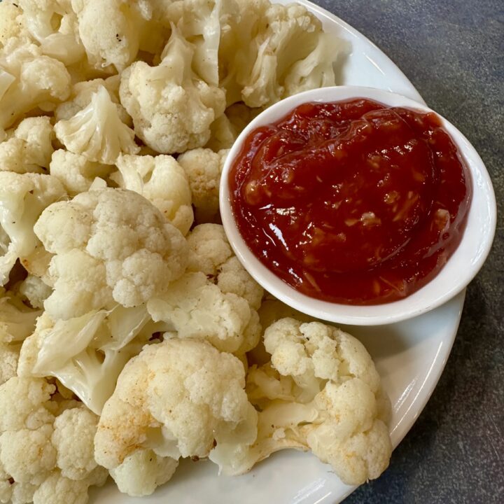 Boiled Cauliflower on a white plate with a side of ketchup based cocktail sauce