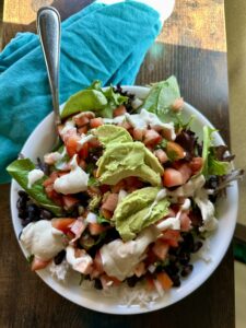 TAco bowl with white rice, black beans, pico de gallo, cashew sour cream and avocado in a white bowl on a table with a blue napkin