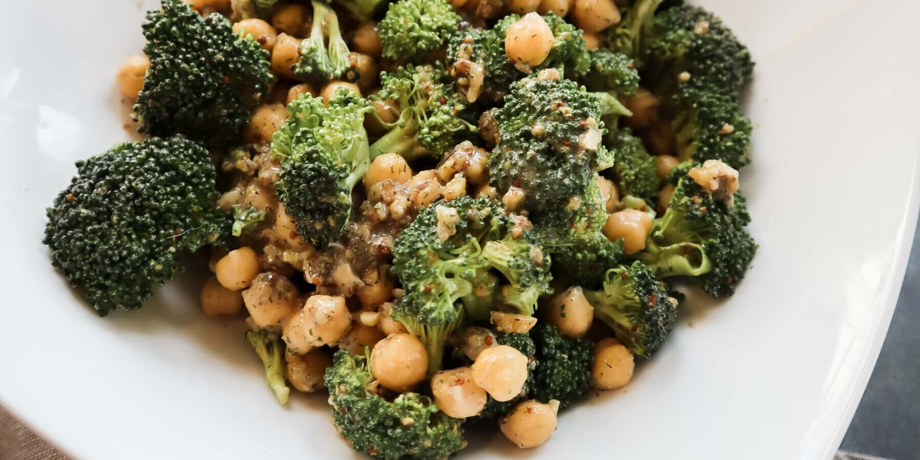 broccoli, walnuts, and chickpeas mixed i white bowl with mustard dressing photographed on cloth next to super easy plant-based cookbook