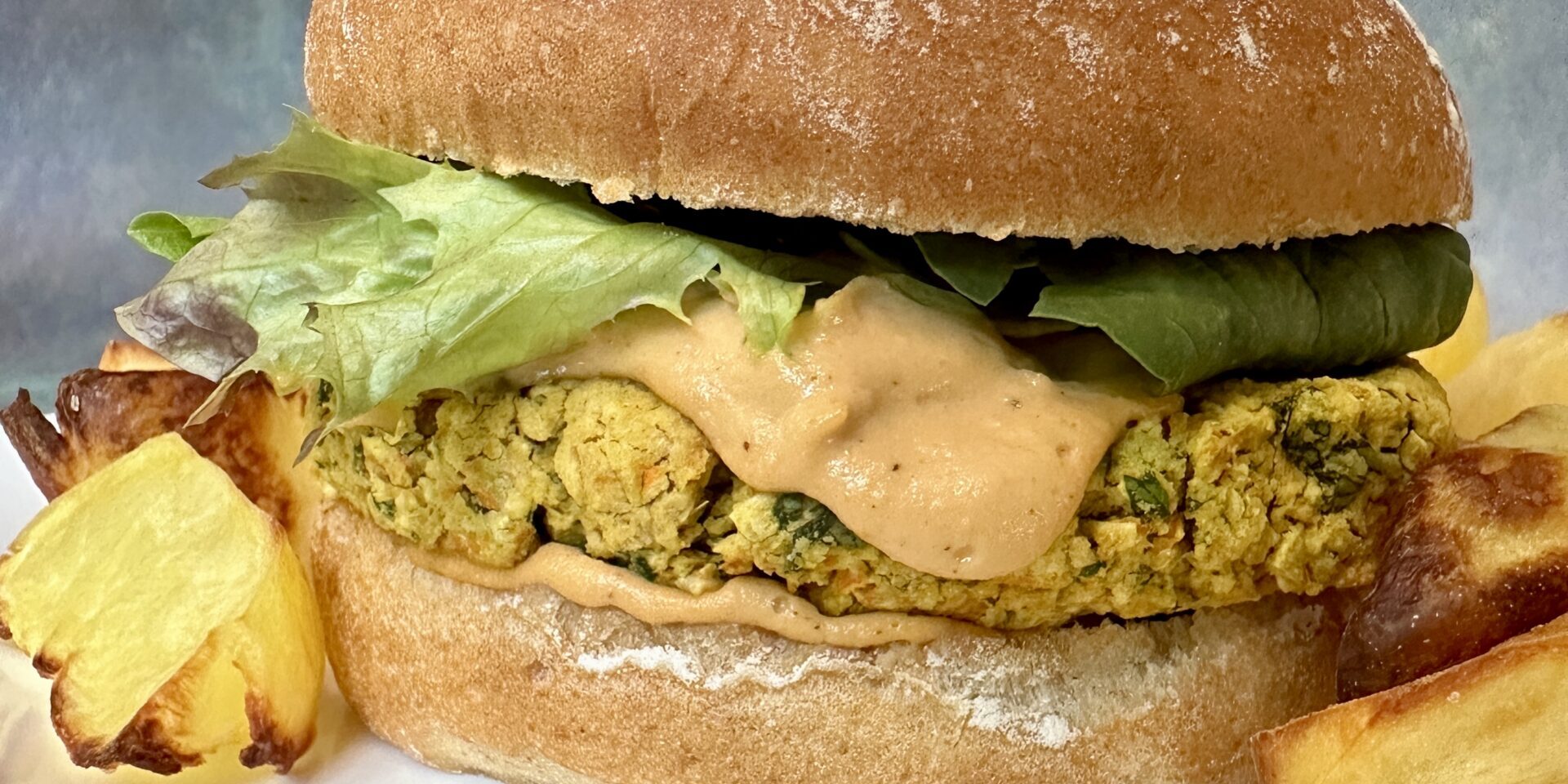 Chickpea basil burger on a bun with roasted potatoes on a white plate