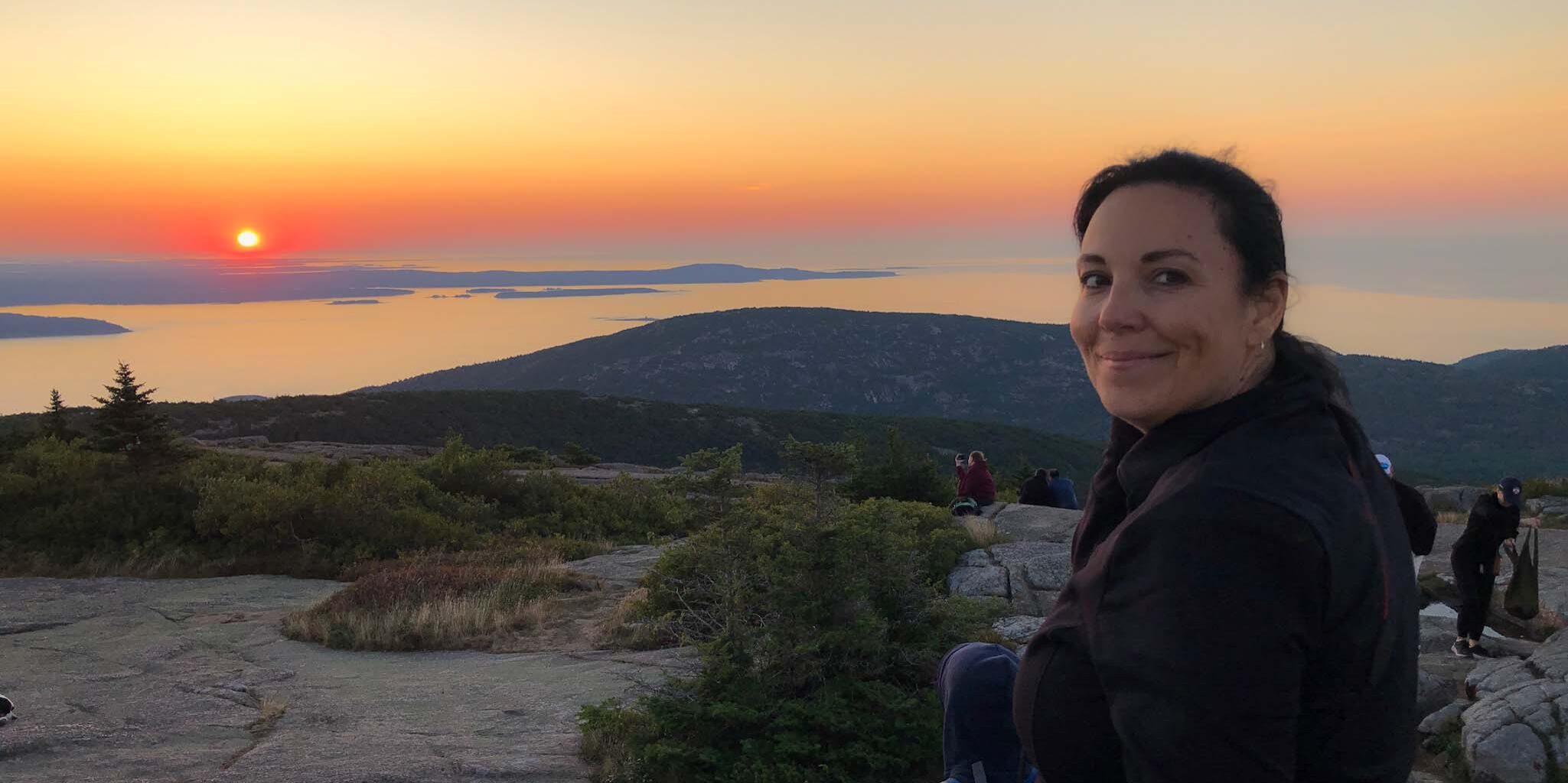 Kathy - VegInspired - woman sitting on mountain overlooking ocean at sunrise